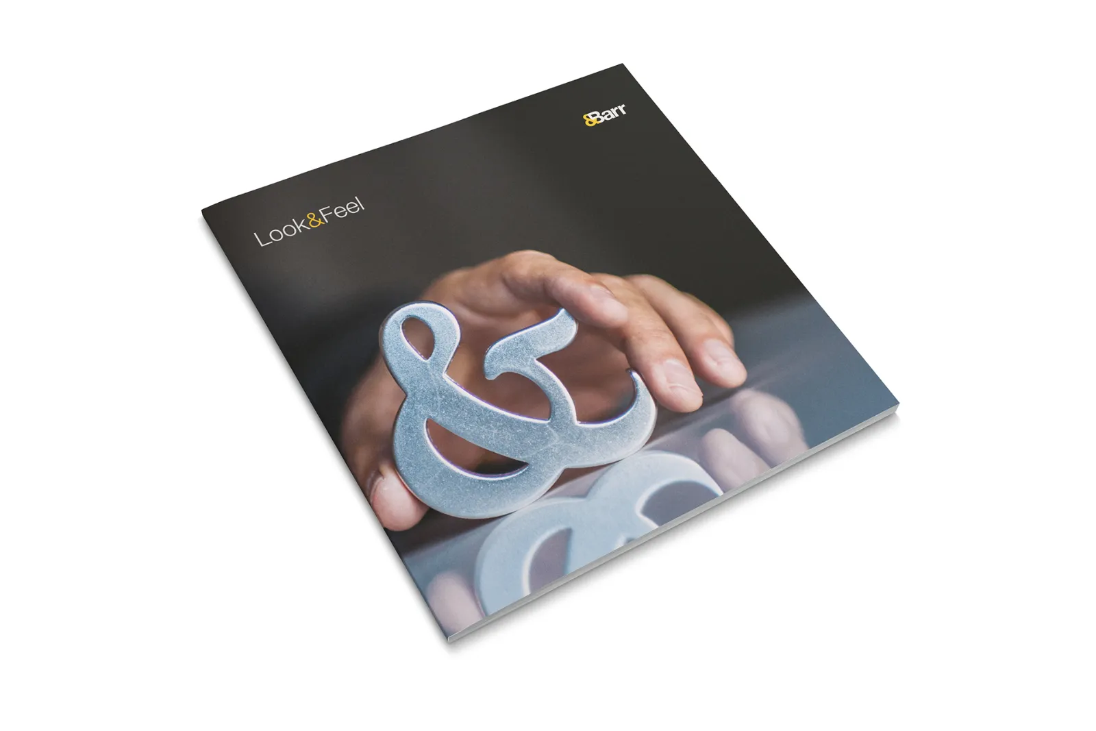 The &Barr Look and Feel culture book, with a hand holding a large ampersand on the cover