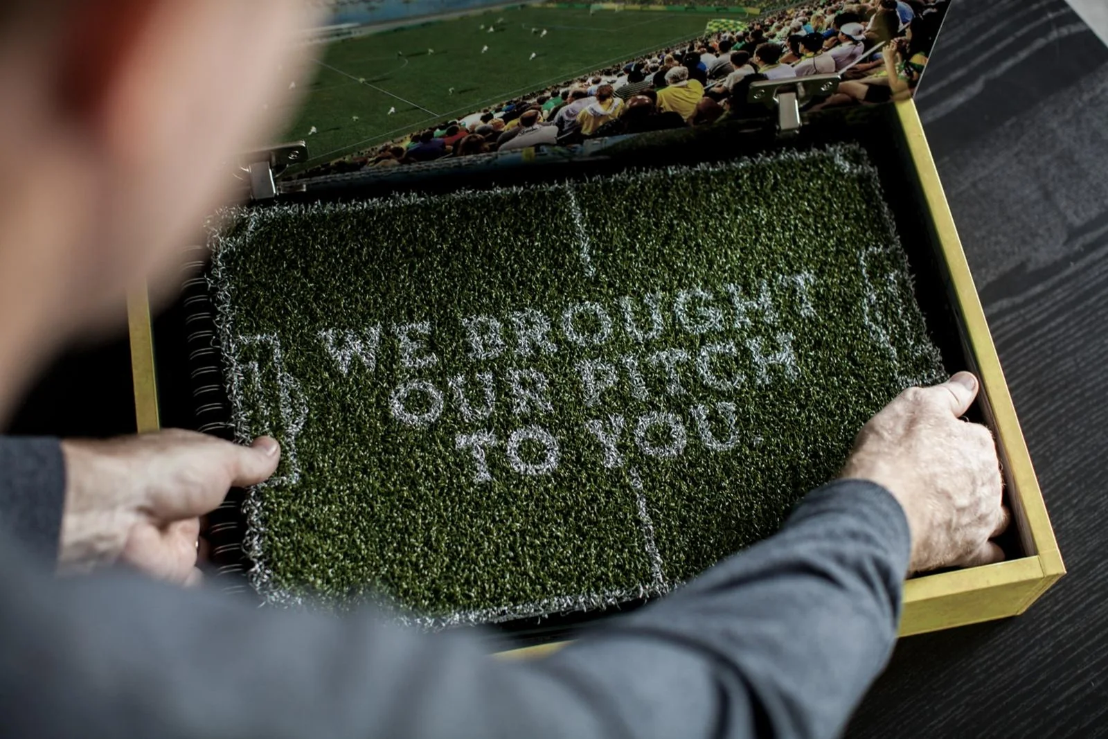 A hand opens the gold Rowdies application box, lined with turf that reads We brought our pitch to you